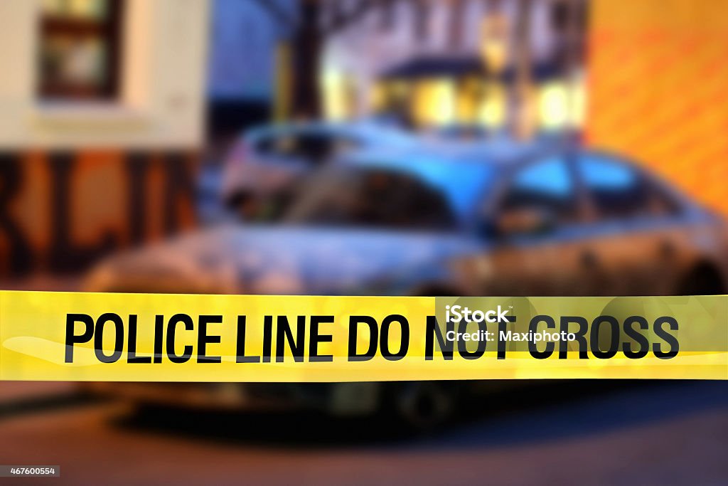 Police line do not cross: car on street at night "Police line do not cross" yellow plastic tape marks the boundary to a restricted area in a city downtown at night, with a blurred parked car in the background, where police forces are investigating crimes or accidents and performing their duties. Outdoor crime scene. Copy space on image top side. 2015 Stock Photo