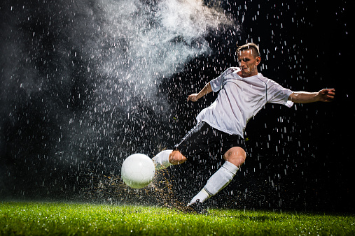 Soccer player kicking a ball while playing soccer on the football pitch in the rain.
