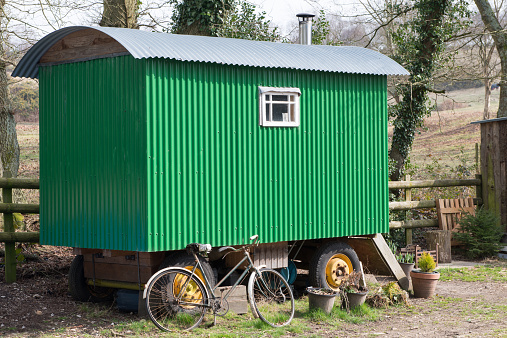 A traditional shepard 's hut in the New Forest Hampshire, England.  It is a sunny early spring day. The hut is made of corrugated iron and painted green.