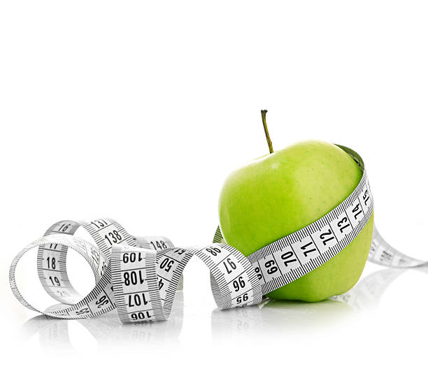 fita de medição envolvidos em torno de uma maçã verde - weight apple loss weightloss imagens e fotografias de stock