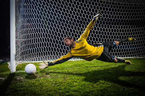 Soccer goalie jumping for a ball while defending his goal.