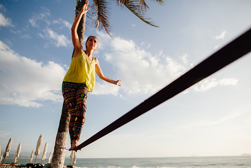 teenage girl  balancing on slackline with sky view on the beach