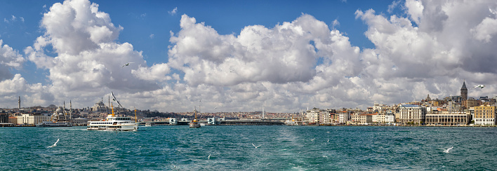 Panoramic view over ferries arriving on the shore of Halic or Golden Horn, from the Bosphorus in Istanbul, Turkey on a beautiful day. The Karakoy district with the Galata tower are on the right in the background. And the new Mosque and Fatih Mosque are on the left. The ferry connects the European side to the Asian side of Istanbul.