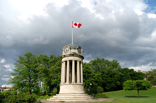 Canadian flag on clock tower with gray clouds The clock tower in Kitchener's Victoria Park with the Canadian Flag against a dark storm clouds. Nice summer scene with sunlight illuminating clock tower for great contrast. kitchener ontario photos stock pictures, royalty-free photos & images