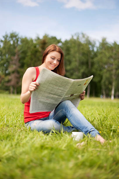 istock Woman sits on a grass and reads the newspaper 467635510