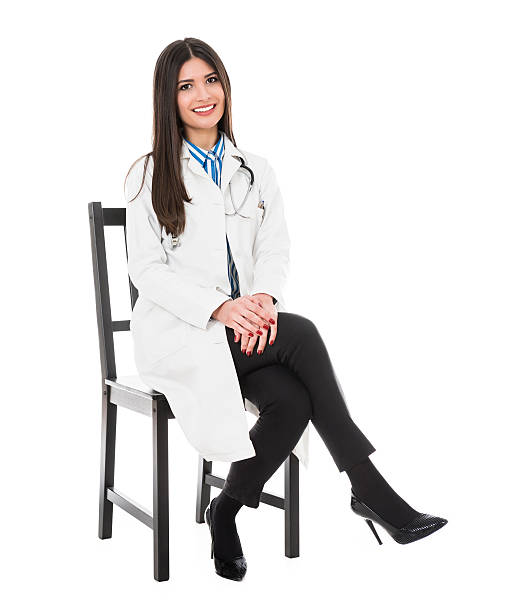 Young Attractive Female Doctor how Smiling and Sitting on Chair Young Attractive Female Doctor how Smiling and Wearing Medical Uniform and sitting on chair. Isolated on White. woman sitting cross legged in chair stock pictures, royalty-free photos & images