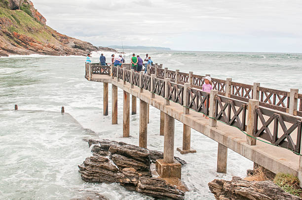 Bramwell Butler Pier at Victoria Bay George, South Africa - January 3, 2015: Unidentified people on the Bramwell Butler Pier at Victoria Bay. Train tunnel visible left top george south africa stock pictures, royalty-free photos & images