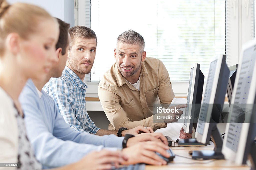Adult education Group of adult students attending computer course. Focus on the smiling male teacher pointing at computer screen. Adult Student Stock Photo
