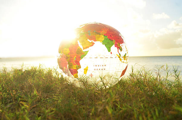 transparent globe on grass and bright sunbeam picture of brightly lit transparent globe showing Africa and Asia. Globe rests on grass against a beach backdrop with horizon. Horizon is aligned with the equator on the globe.  equator line stock pictures, royalty-free photos & images