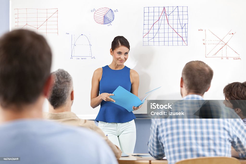 Adult Ed Group of adult student attending a job training. Focus on female teacher standing with notebook in front of whiteboard. Note Pad Stock Photo