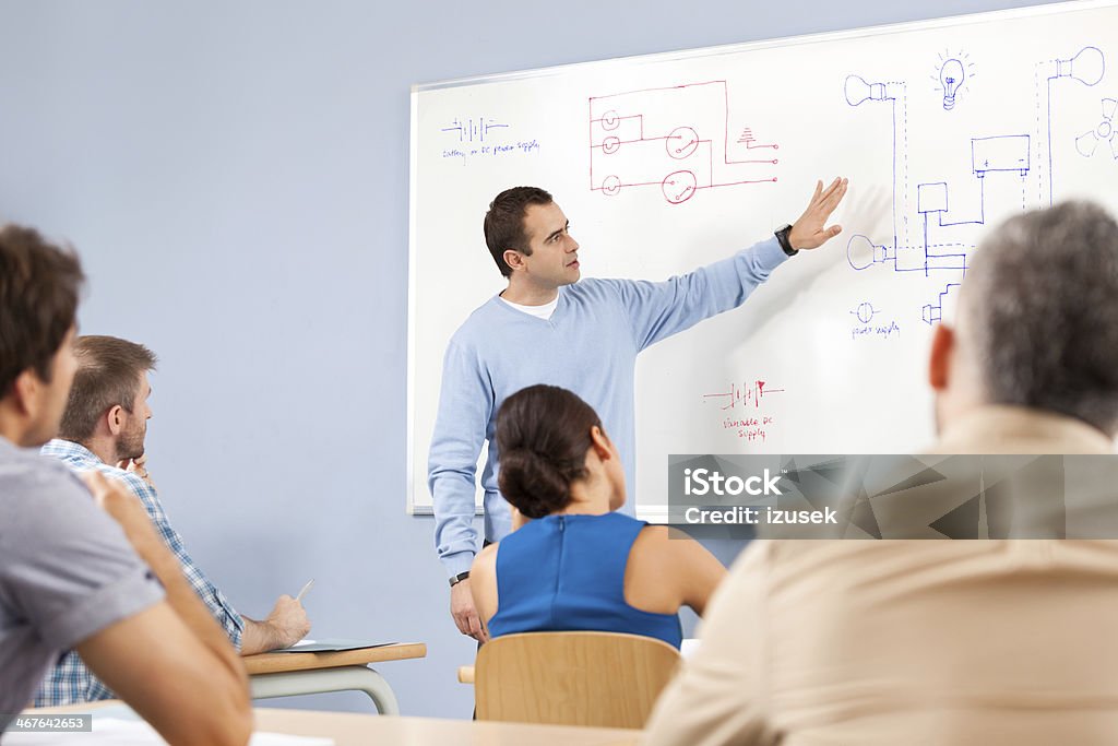 Job training Group of adult student attending a job training. Male teacher explaining diagrams technical systems drawn on whiteboard. Education Training Class Stock Photo