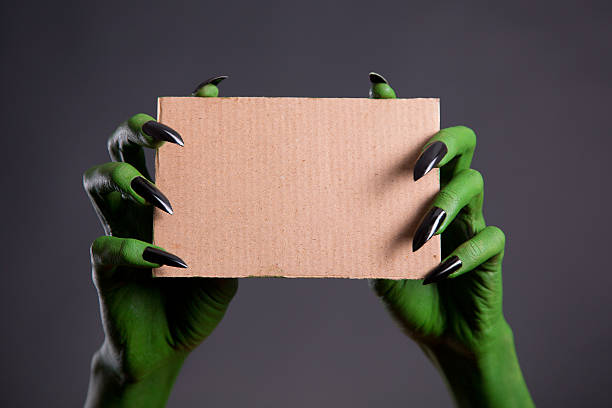 istock Green hands with black nails holding empty piece of cardboard 467645402