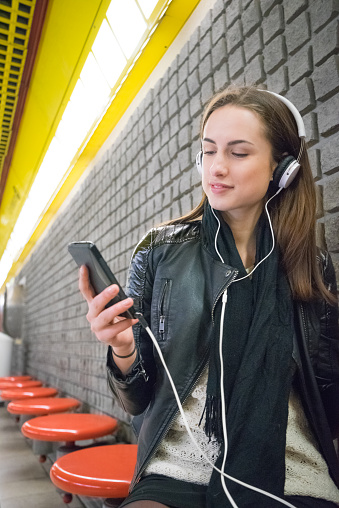 Beautiful woman listening to music from her smartphone, subway station background.