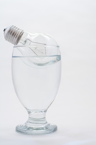 A light bulb floating atop a full glass of water with a white background.
