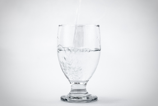 Water being poured into a half full glass with a white background.