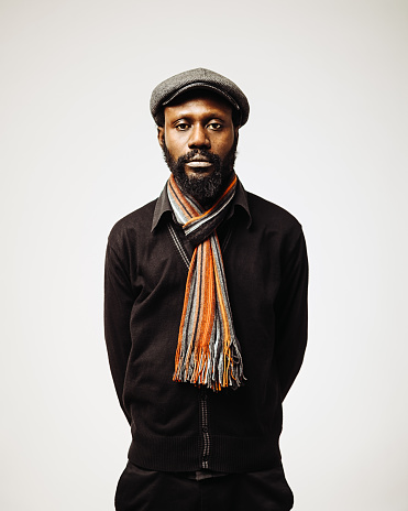 Portrait of a bearded elegant afro american man wearing a scarf and a cap. Sharp focus on eyes. Studio shot and white background. Sharp focus on eyes.