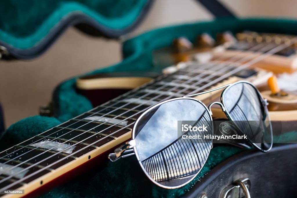 Sandy Guitar With Sunglasses When it's time to relax, there are few things better than sitting on a beach (or on the rooftop of your beach resort) with a guitar.  These items are the epitome of getting away and relaxing, even if you can never quite get all the sand off of your guitar. 2015 Stock Photo