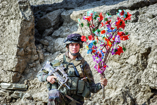 Kaboul, Afghanistan - August 20, 2010: The picture was took in the capital of Afghanistan during a morning time, we can see a french soldier from troupes of marines, he pose and looking at the camera, happy of the end of the war he is keeping a colorful flower of liberty in one hand and his weapon in the other. August 2010