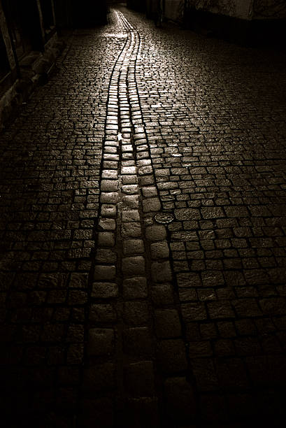 A dark cobble stone street light by a lone light source.