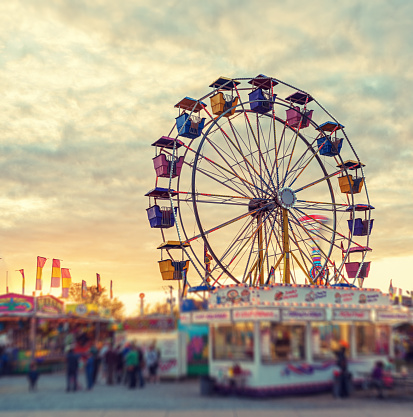 A large ferris wheel pauses to reload in sunset light at a small midway.  Tilt shift lens effect.
