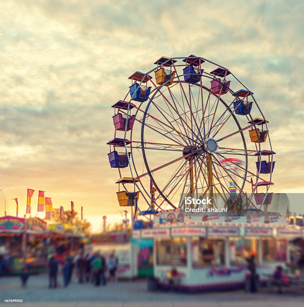 Sunset over the Midway A large ferris wheel pauses to reload in sunset light at a small midway.  Tilt shift lens effect. Traveling Carnival Stock Photo