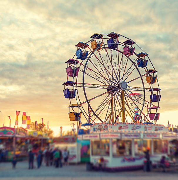 Sunset over the Midway A large ferris wheel pauses to reload in sunset light at a small midway.  Tilt shift lens effect. midway fair stock pictures, royalty-free photos & images