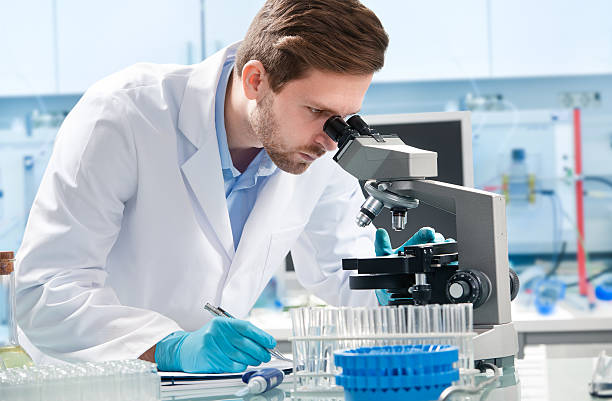 naukowiec patrząc przez mikroskop - scientist research test tube lab coat zdjęcia i obrazy z banku zdjęć