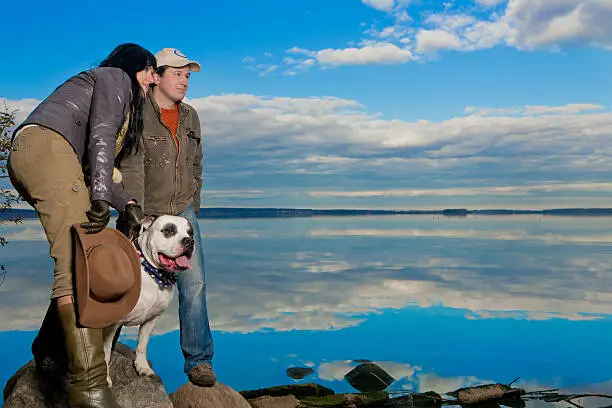 young and attractive positive looking country family with their big nice dog standing together and looking appear against amazing blue sky background and superb mirror water reflection.shoot made on location using strobe flash