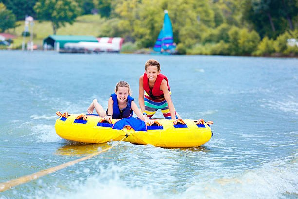 брат и сестра детей игривым трубки на озеро воду, наслаждаясь летние каникулы - water sport family inner tube sport стоковые фото и изображения