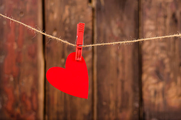 One red heart hanging on the clothesline. Old wood background. stock photo