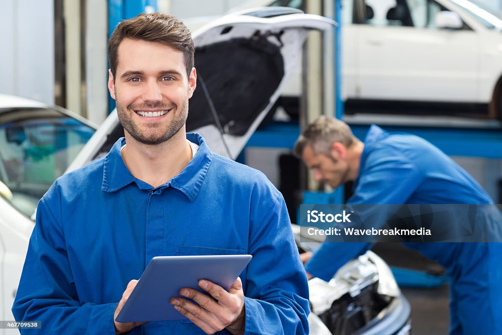 Young man using a tablet in a mechanic's workshop Smiling mechanic using a tablet pc at the repair garage Mechanic Stock Photo