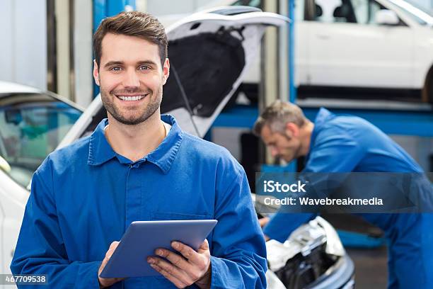 Young Man Using A Tablet In A Mechanics Workshop Stock Photo - Download Image Now - Mechanic, Auto Mechanic, Auto Repair Shop