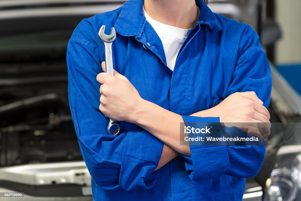 Mechanic in an automotive garage holding a wrench Mechanic holding wrench with crossed arms at the repair garage Mechanic Stock Photo