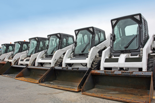 Multi purpose mini loaders equipped with  scoops,  ready for snow removal in a large parking lot.