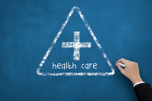 A woman's hand is drawing a health care symbol on blue chalkboard from the bottom.