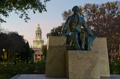 Waco, United States - November 29, 2013: A bronze statue of Judge Baylor overlooks a garden of roses, leading to Pat Neff Hall, the main administrative building with a bell tower in the background.  A dusky sunset falls over Waco, Texas and the campus of Baylor University.