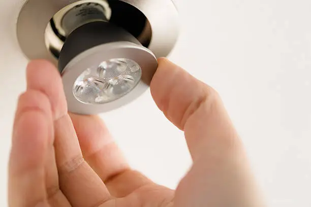 A male hand is installing a LED light bulb into a ceiling can fixture.