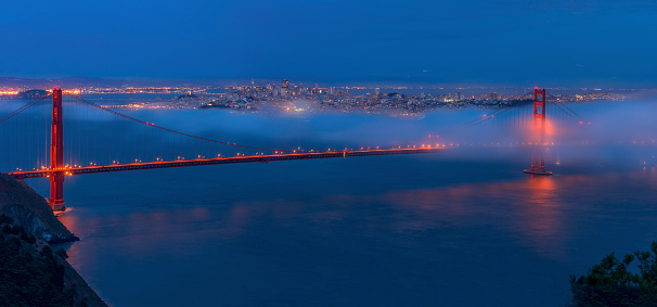 Golden gate bridge with low fog after sunset. Downtown and bay bridge on the background. Multiple stitch.