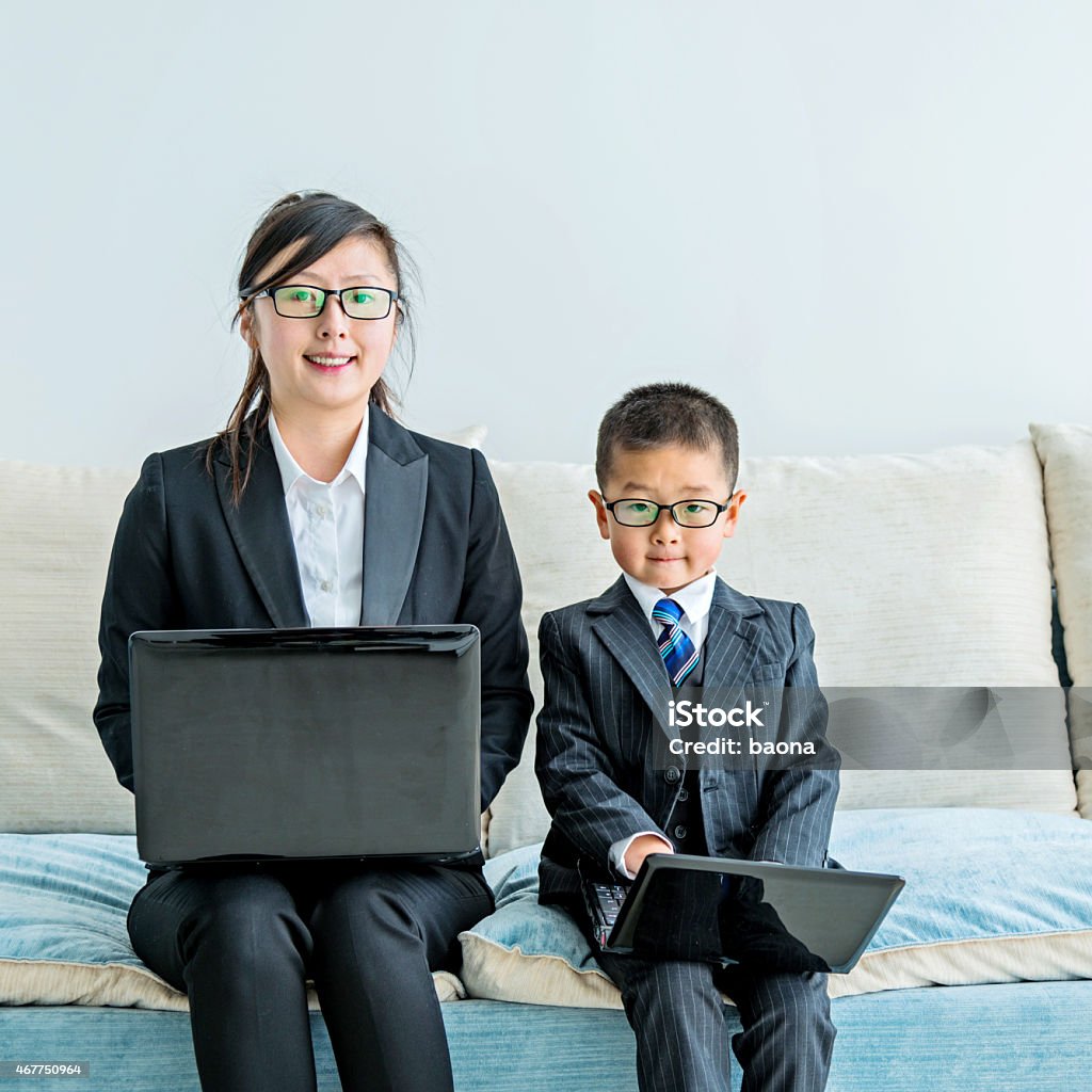 Businesswoman and her little son working together Businesswoman and her son holding their laptop and sitting on sofa at home. 2015 Stock Photo