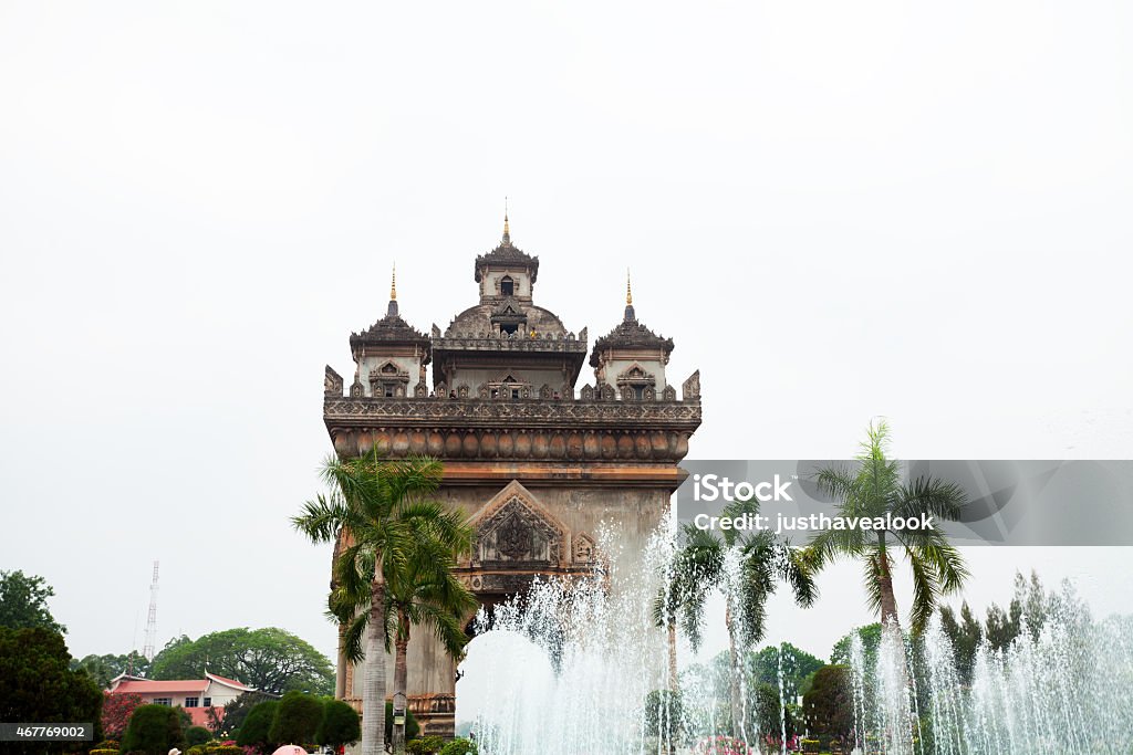 Victory monument Patuxai and fountain in Vientiane Dayshot of victory monument Patuxai (ປະຕູໄຊ, Monument des Morts) and fountain in Vientiane. On top of gate are tourists. 2015 Stock Photo
