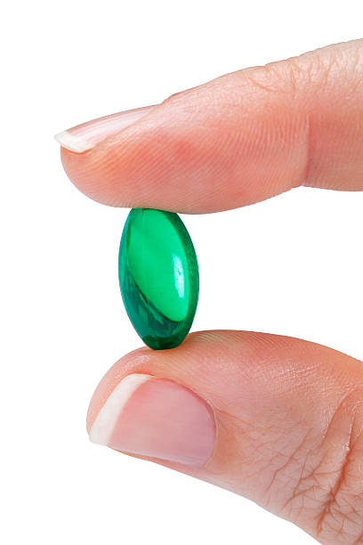 istock Small green semi transparent pill between two fingers 467769219
