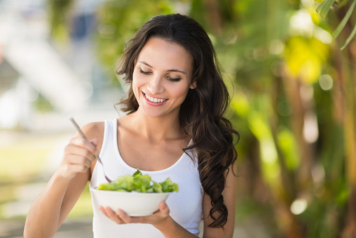 Pretty brunette eating bowl of salad on a sunny day