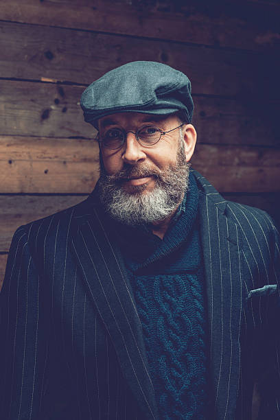 Close up Portrait of a Smiling Middle Age Goatee Man with Eyeglasses Wearing an Elegant Wear In Front a Wooden Wall While Looking at the Camera.