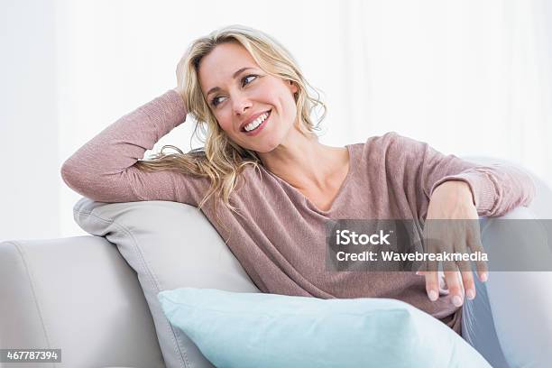 Blonde Sitting On Couch Smiling And Thinking Stock Photo - Download Image Now - Mid Adult Women, 2015, 30-39 Years