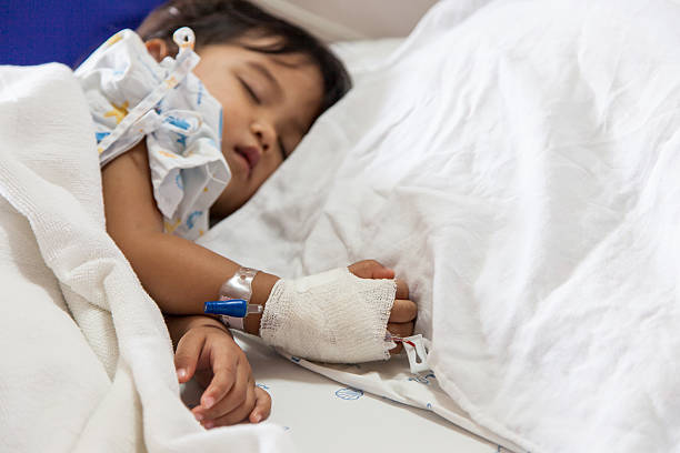 Sick child asleep in hospital bed with gown and canula Close up of hand children sick sleeping on the bed to the brine on hand for treated at hospital saline drip stock pictures, royalty-free photos & images