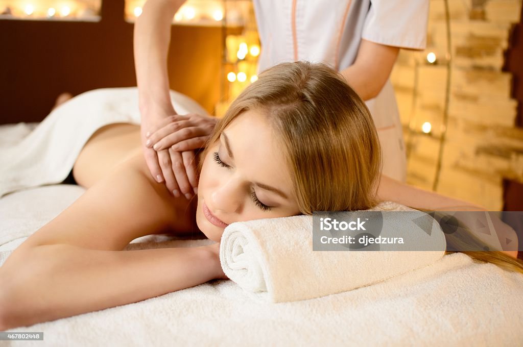 Young beautiful woman lying on a massage table Young beautiful white  woman lying on a massage table and is being massaged Back Stock Photo