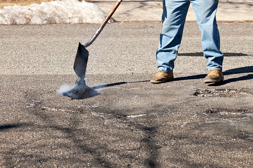 Road worker shoveling and dumping hot asphalt repairing road, filling potholes in middle of street.  Motion blur on shovel and asphalt. Photo taken  in daylight with Canon 5D Mark2 at 100 ISO, 70-200mm lens at 145mm f9, 1/200 sec.