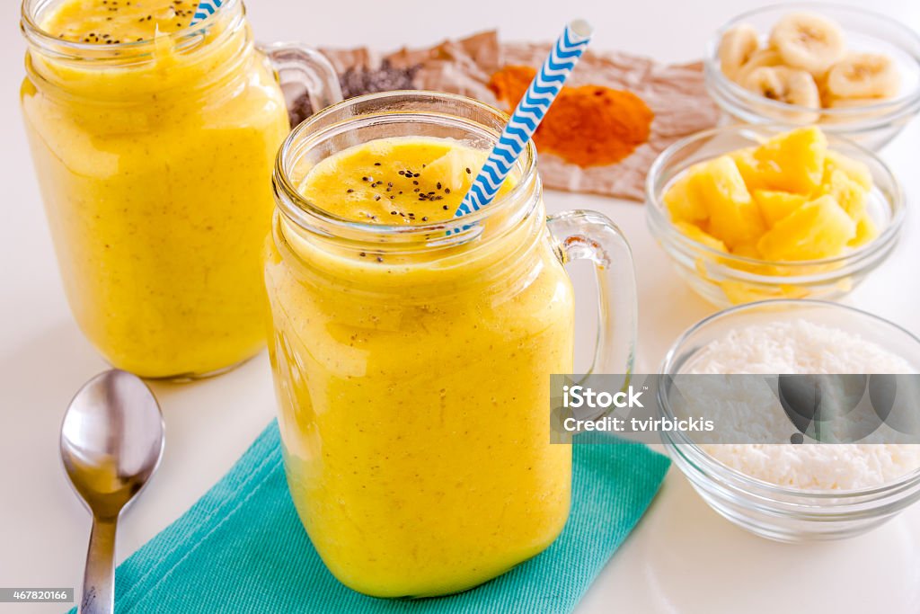 Pineapple, Banana, Coconut, Turmeric and Chia Seed Smoothies Fresh blended fruit smoothies made with pineapple, banana, coconut, turmeric and chia seeds surrounded by raw ingredients with blue straws 2015 Stock Photo