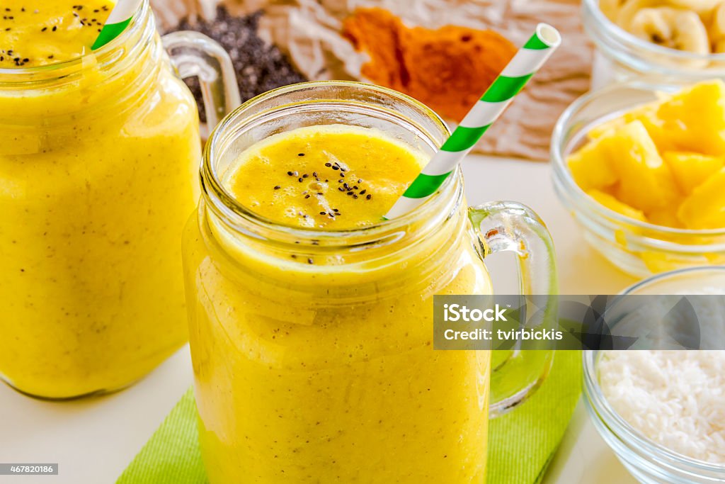 Pineapple, Banana, Coconut, Turmeric and Chia Seed Smoothies Close up of fresh blended fruit smoothies made with pineapple, banana, coconut, turmeric and chia seeds surrounded by raw ingredients green straws 2015 Stock Photo