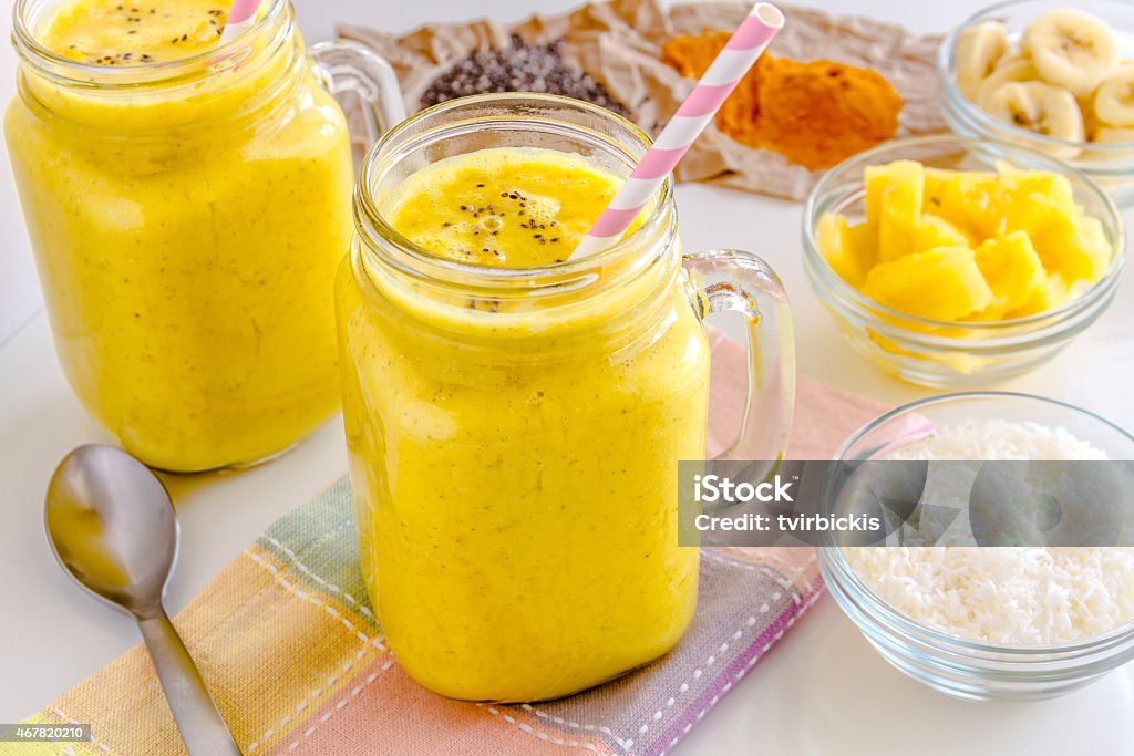 Pineapple, Banana, Coconut, Turmeric and Chia Seed Smoothies Fresh blended fruit smoothies made with pineapple, banana, coconut, turmeric and chia seeds surrounded by raw ingredients pink straws 2015 Stock Photo